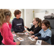 Négy kisgyermek az asztal körül játszik az Animal Chat! kártyajátékkal, közösen nevetve és beszélgetve.