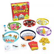 A Hedbanz társasjáték tartozékai: hat különböző fejpánt (cápa, unikornis, katica, villanykörte, virág, űrhajós), kártyák, homokóra és sárga jelzőzsetonok, a háttérben a játéktartó dobozzal.