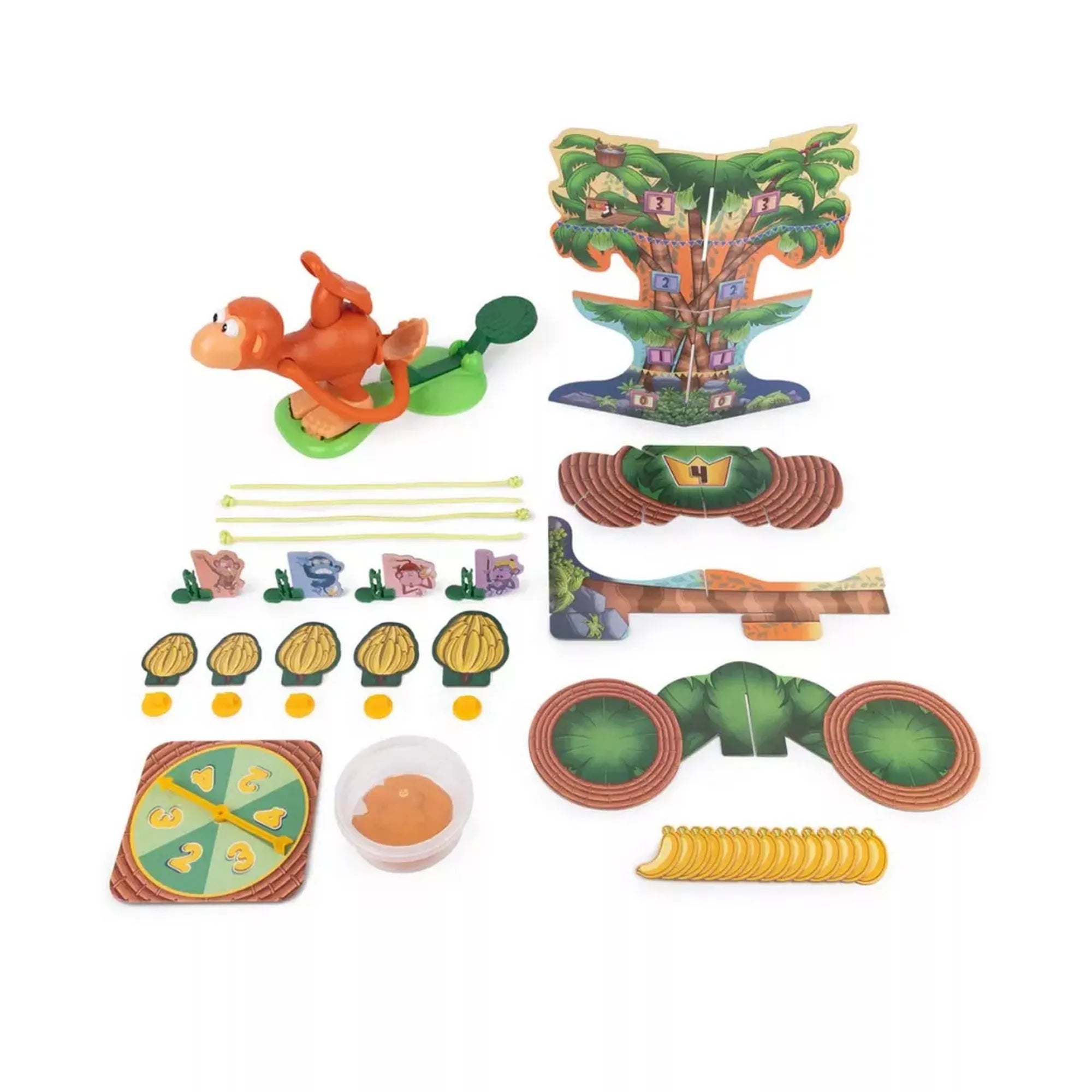 A Monkey See Monkey Poo társasjáték minden tartozéka elrendezve: a narancssárga majom figura, a pálmafás játéktábla elemei, banánkártyák, célpontok, pörgető és egy tálka a játékanyaggal.