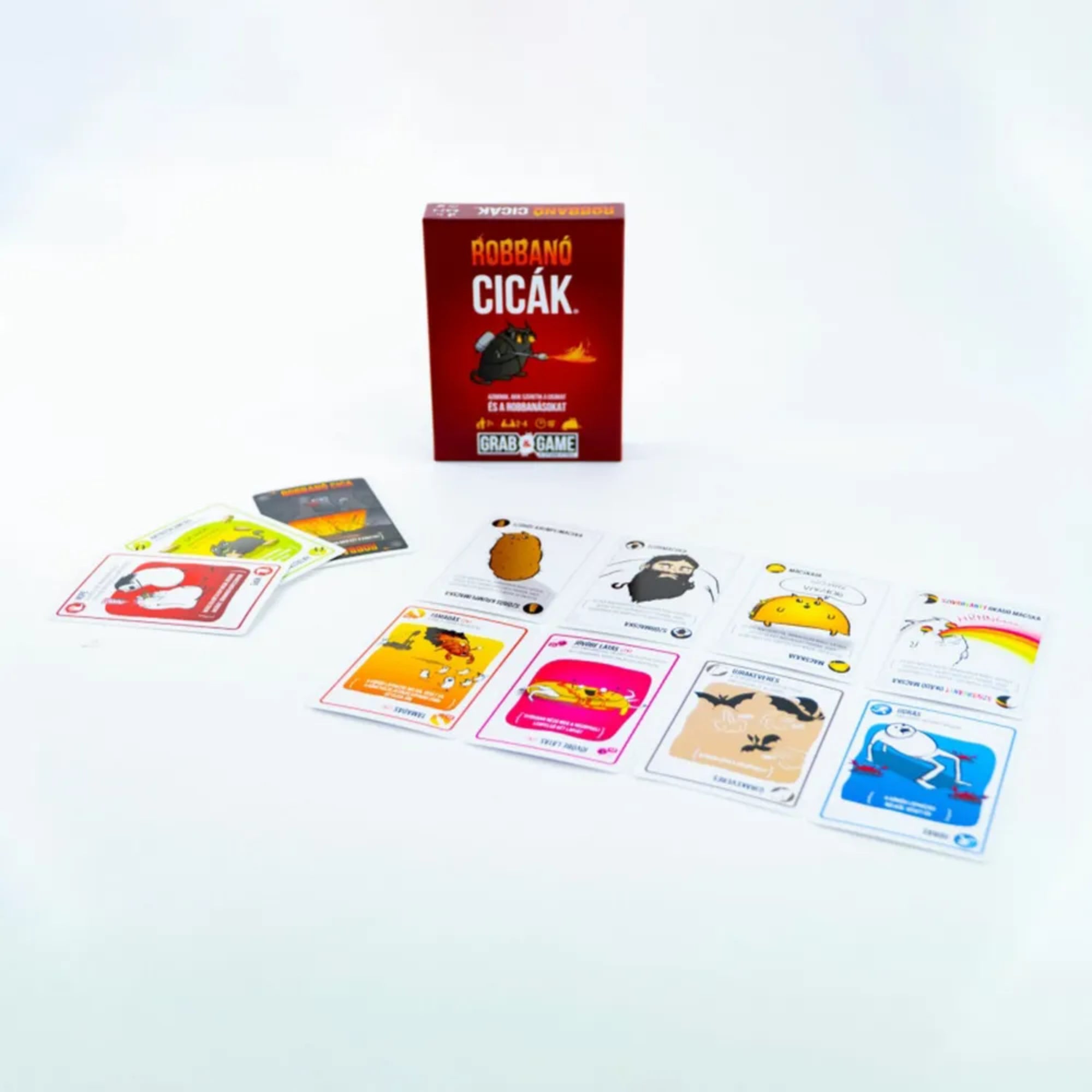 A képen a Robbanó Cicák Mini társasjáték tartalma látható kibontva. Középen helyezkedik el a játék piros színű doboza, rajta a jól ismert lángszórós macskával. Körülötte színes, humoros illusztrációval ellátott kártyák sorakoznak, amelyek mindegyike egyedi akciót vagy karaktert ábrázol – például a „TACOCICA”, a „SZŐRBOCS”, vagy a „SZELLEM CICA”. A különleges kártyák mind a játékosok taktikázását és túlélési esélyeit befolyásolják.