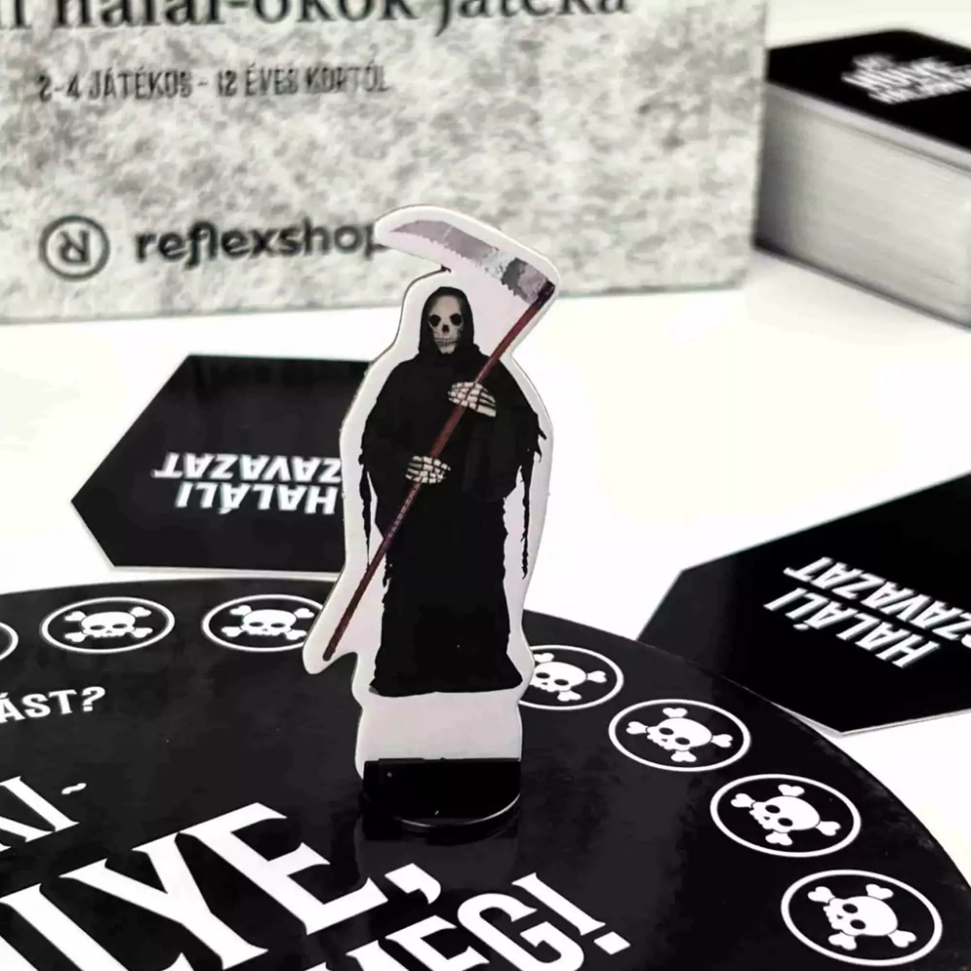 Az Aki hülye, haljon meg! társasjáték kaszás figurája a fekete játéktáblán.
