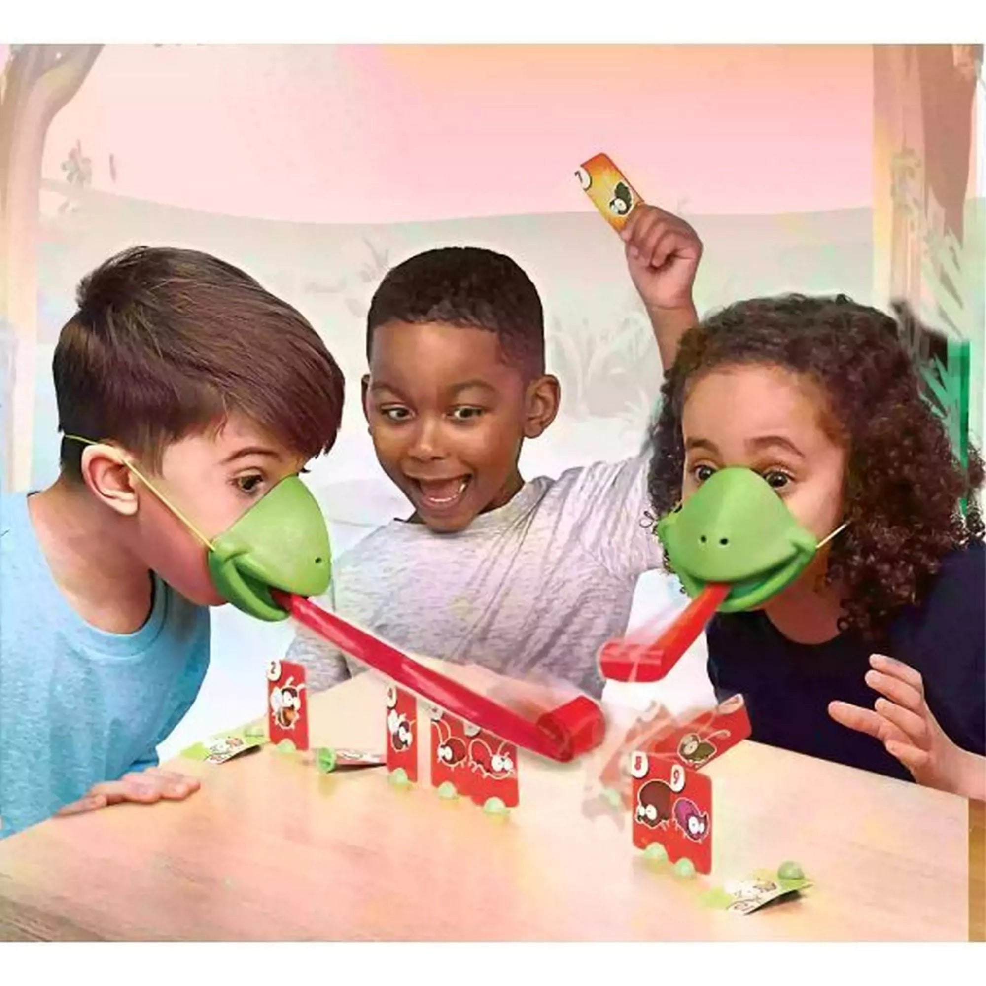 Három gyerek nagy lelkesedéssel játszik, kaméleonmaszkban, miközben a piros nyelvekkel próbálják ledönteni a kártyákat.