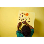 Gyerek felülről nézve a LEGO Spider-Man: A Pókverzum minifigurák teljes kollekcióját rakja ki sárga asztalon.