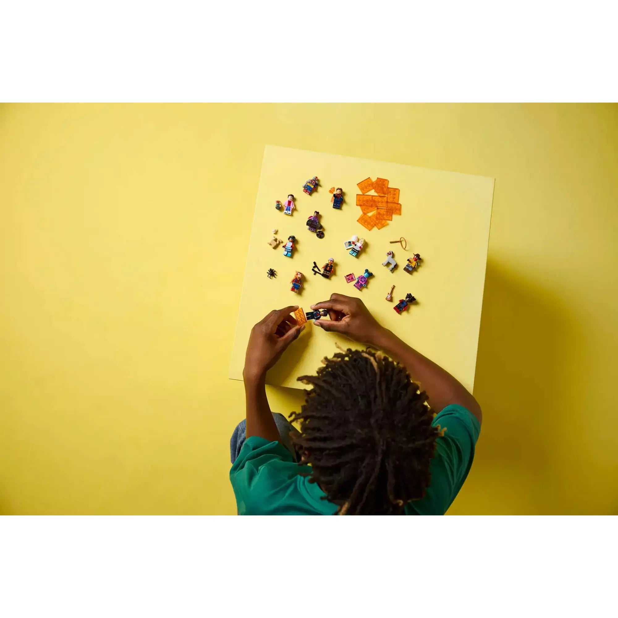 Gyerek felülről nézve a LEGO Spider-Man: A Pókverzum minifigurák teljes kollekcióját rakja ki sárga asztalon.