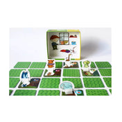 Maszat és az elveszett plüssök társasjáték játéktáblája elrendezett kártyákkal, közöttük álló plüssfigurákkal, a háttérben pedig a nyitott doboz rajzolt belső jelenettel.