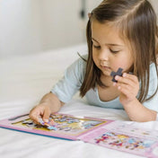 Kislány a Melissa & Doug mágneses kirakó – Hercegnők puzzle darabjait illeszti be a rózsaszín táblába, koncentrált játék közben.