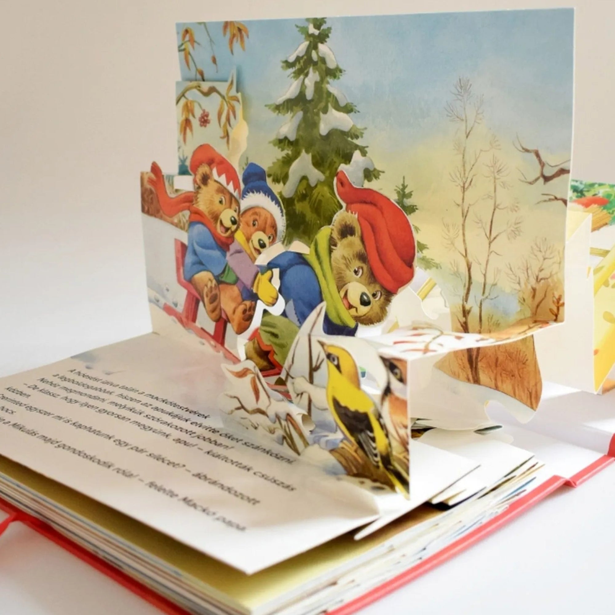 Mesél az erdő – Karácsony kinyitott könyv – A 3D könyv egyik oldalán három medve szánkózik havas tájon, mögöttük téli erdő és fenyőfa látható.