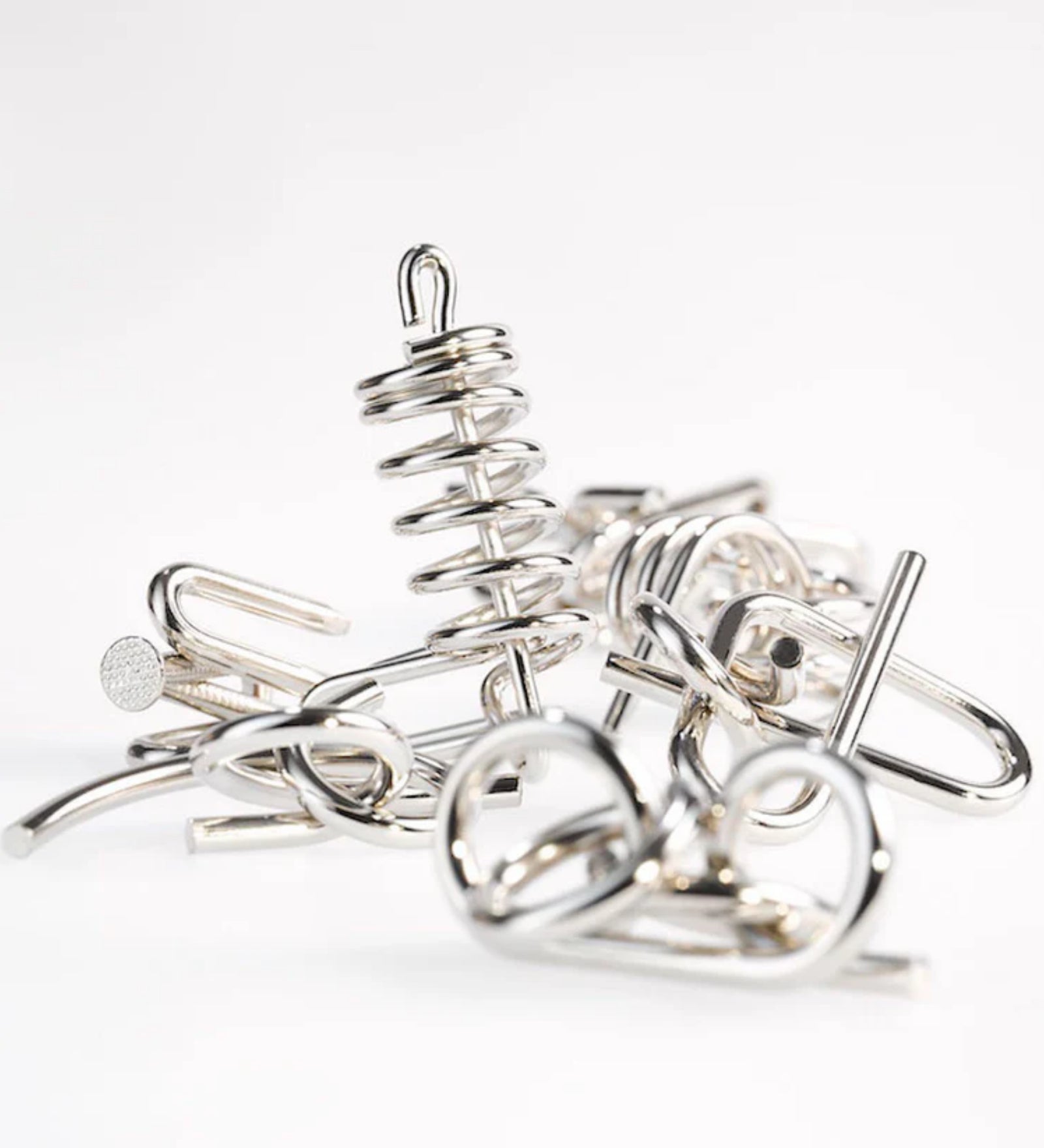 Fémből készült logikai játékok kupaca a 10 Metal Puzzle Set kék kiadásából, változatos mintázatú, fényes felületű drótformákkal, fehér háttér előtt.