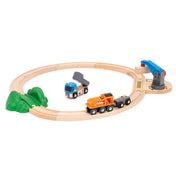 BRIO Kezdő emelő és rakodó készlet elrendezve: A fa sínpályán narancssárga mozdony és kék dömper közlekedik, mellette egy mozgatható daru és zöld domb elem.
