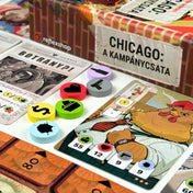 Chicago: A kampánycsata társasjáték részletfotó, karakterkártyákkal, újságkártyával és színes jelölőkorongokkal, amelyek különböző akciókat és erőforrásokat jelölnek.