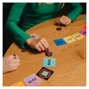 Hitster zenei társasjáték játék közben: játékosok egy faasztal körül idővonalba rendezik az évszámos kártyákat, miközben egy QR-kódos kártyát helyeznek le a sorba.