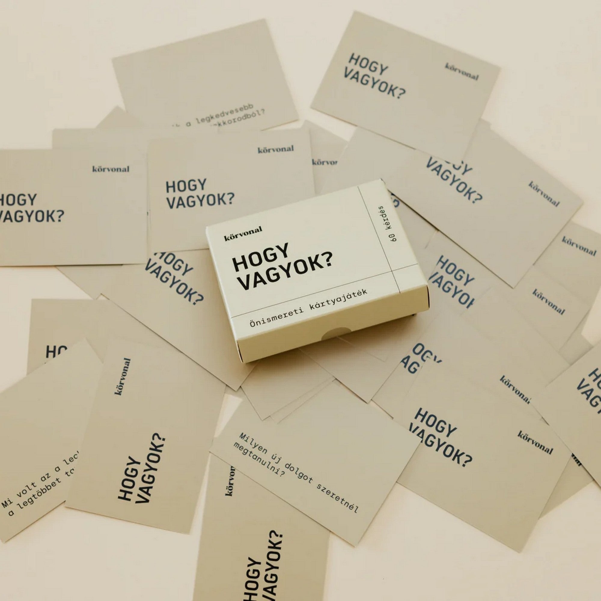 A Körvonal – Hogy vagyok? önismereti kártyajáték kiterített lapjai, középen a dobozzal, amely 60 kérdést tartalmaz az önismeret fejlesztéséhez.