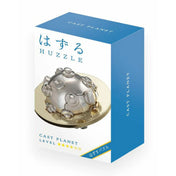 A Huzzle Cast PLANET doboza, fehér-kék színvilággal, középen a kirakott puzzle képe: egy ezüst színű csavarokkal tarkított gömb egy arany színű, fogazott gyűrű közepén.

