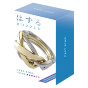 A Huzzle Cast RING dobozakék-fehér dizájnnal, rajta a puzzle elegáns, fonott gyűrűformája és a nehézségi szintet jelző csillagok.