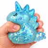 Kézben összenyomott kék, csillámos unikornis squishy stresszlevezető játék fehér háttér előtt