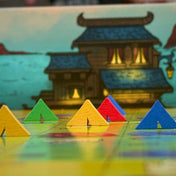 Kóborló Karaván – Színes sátorjelölők a játéktáblán, előtérben fa figurák, háttérben épületgrafika.