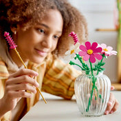 LEGO Botanicals Kozmoszvirágok (11514) építőkészlet használat közben, ahol egy gyermek a színes LEGO virágokat rendezi egy áttetsző üvegvázában.