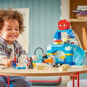 LEGO DUPLO Marvel Pókember csapata főhadiszállása 10464 játék közben, ahol egy kisgyermek a Pókemberes főhadiszállással, csúszdával és szuperhős figurákkal játszik.