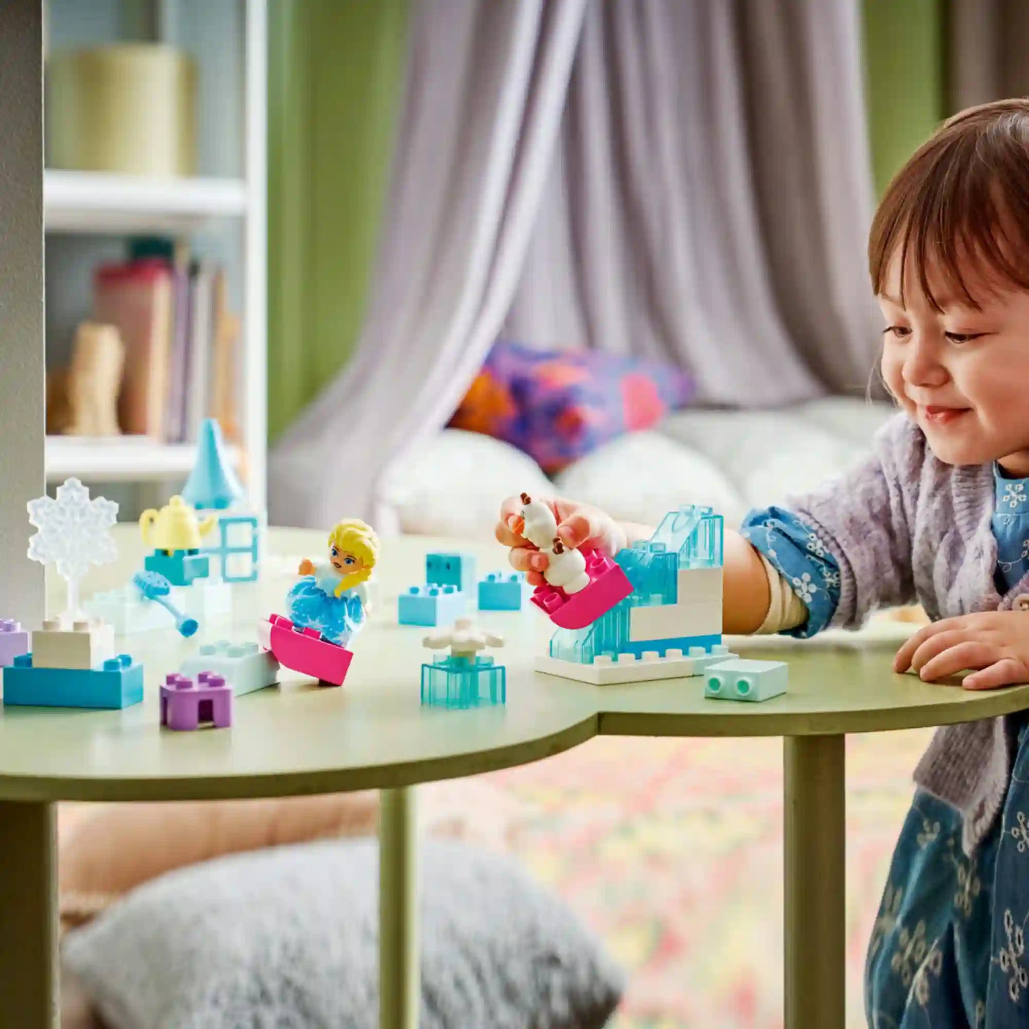 LEGO DUPLO Disney Jégvarázs Elsa és Olaf kreatív építőkészlet (10462) használat közben, kisgyermek által épített Jégvarázs jelenetekkel, Elsa és Olaf figurákkal egy játékasztalon.