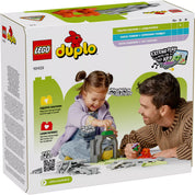 LEGO DUPLO Kiegészítő készlet - Alagút és Vasúti Sínek (10425) dobozának hátoldala, amelyen egy mosolygó kislány játszik egy alagút és sínek összeállításával egy felnőtt segítségével, ösztönözve a kreativitást és a finommotorikus készségek fejlesztését.