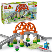 LEGO DUPLO Vasúti híd és sínkészlet, amely tartalmaz egy narancssárga ívhidat, sínpályát, emelhető sorompót, egy vasúti mérnök figurát és további kiegészítőket a kreatív játékhoz, dobozával együtt bemutatva.