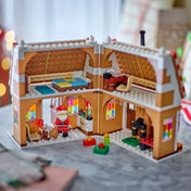 LEGO 40809 Ünnepi mézeskalács ház – A kinyitott mézeskalács ház belső tere látható hálószobával, asztallal, kandallóval, színes ablakokkal és Mikulás minifigurával.