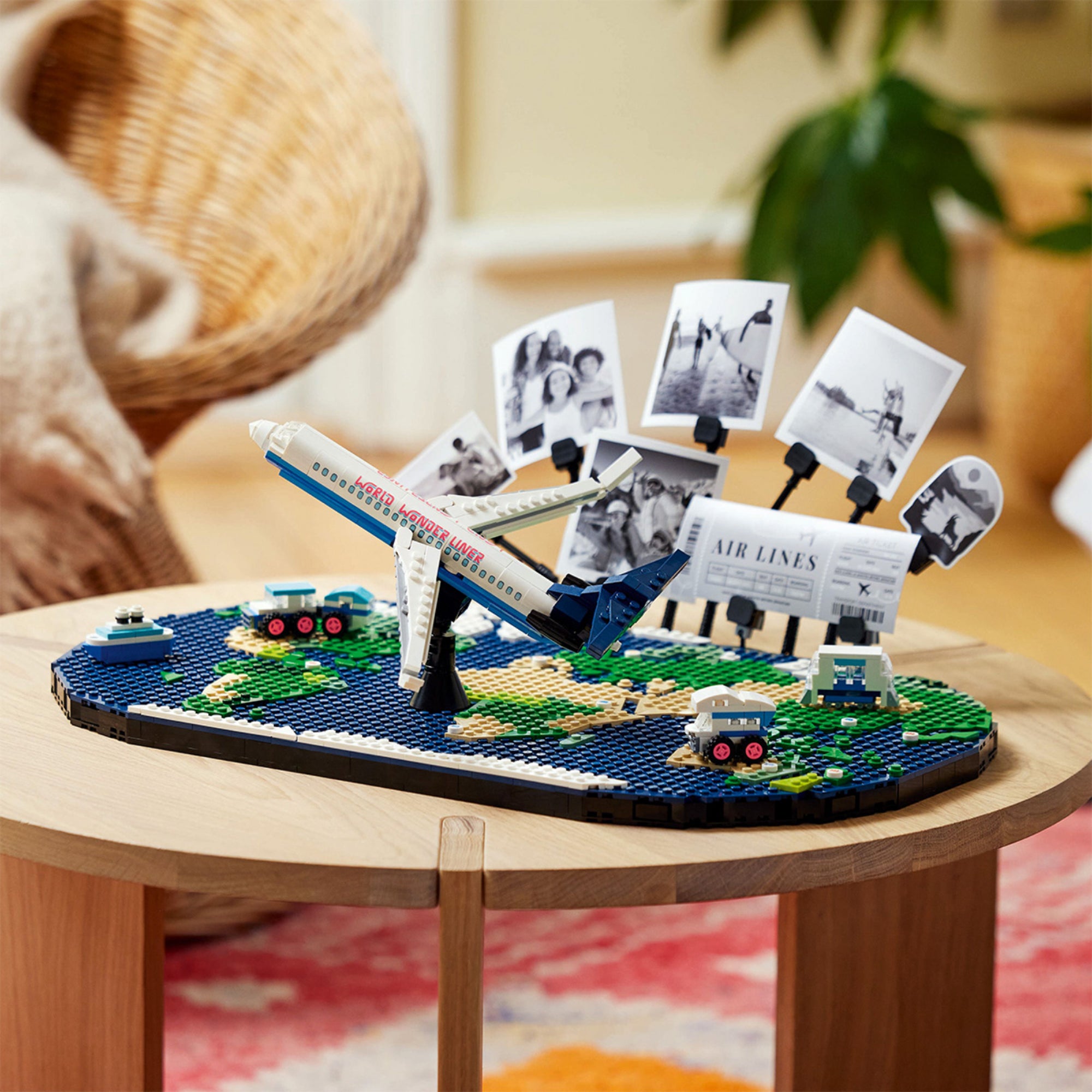 A LEGO Family A nyaralás pillanatai (41838) készlet kiállítva egy asztalon – a világot ábrázoló LEGO alaplap közepén repülőgép, körülötte miniatűr járművek és fényképek.