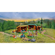 LEGO Friends Otthonos kabinok a kalandtáborban készlet részletes erdei jelenete két faházzal, tábortűzzel, két kerékpárral, magas fenyőfával és három minibaba figurával. A táborban egy rókafigura és számos kiegészítő is látható.