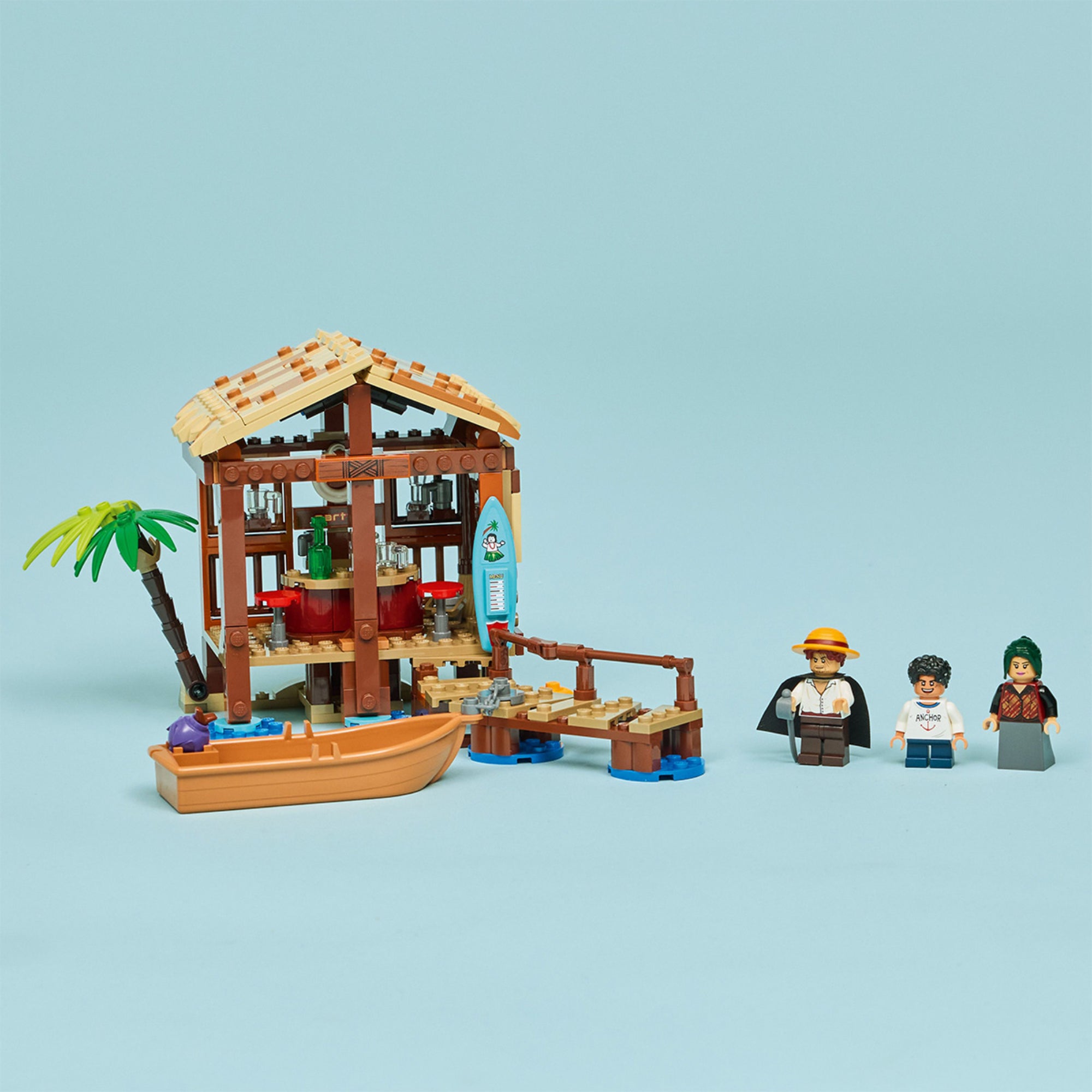 A LEGO One Piece: Windmill Village Hut (75636) készlet részletes képe a világoskék háttér előtt, a kunyhóval, a kis csónakkal és a három minifigurával: Luffy, Shanks és Makino.