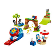 A képen a LEGO Sonic the Hedgehog – Sonic’s Speed Sphere Challenge (76990) készlet egyes elemei láthatók részletesen, összeépítve. A középpontban egy barna-zöld árkádos kapu szerepel, amely alatt három aranygyűrű található – ezek Sonic ikonikus gyűrűi. A kapu tetején egy piros-sárga robot madár helyezkedik el. Jobbra egy zöld rámpa áll, amelyet Sonic sebességgömbje használhat ugratásra.Bal oldalon egy piros-kék kilövő szerkezet található, nagy sárga csillaggal a tetején, mellette pedig egy kis pihenőhely.