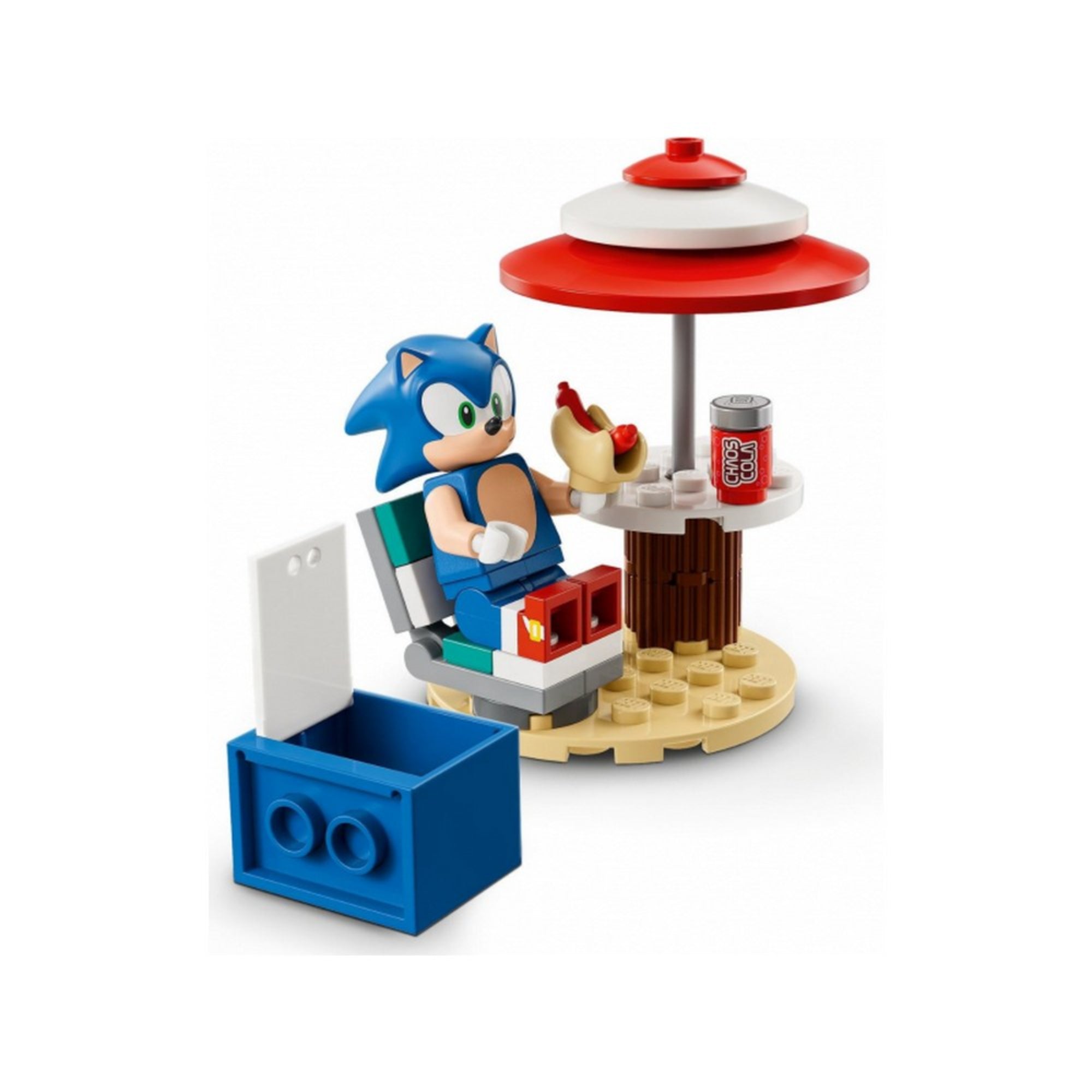 A képen a LEGO Sonic the Hedgehog – Sonic’s Speed Sphere Challenge készlet egyik aranyos jelenete látható közelről. Sonic, a híres kék sündisznó egy napernyő alatt pihen, kényelmes nyugágyban ülve. A kezében egy hot dogot tart, mellette pedig egy kólásdoboz található, amelyen a felirat: Chili Cola. A kis asztalon minden elfér, amit egy gyors szünethez kívánhat.