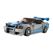 A LEGO Speed Champions Nissan Skyline GT-R (R34) elölnézeti fotója, a volán mögött Brian O’Conner minifigurával, kék-fehér fényezéssel és agresszív hűtőrács kialakítással.