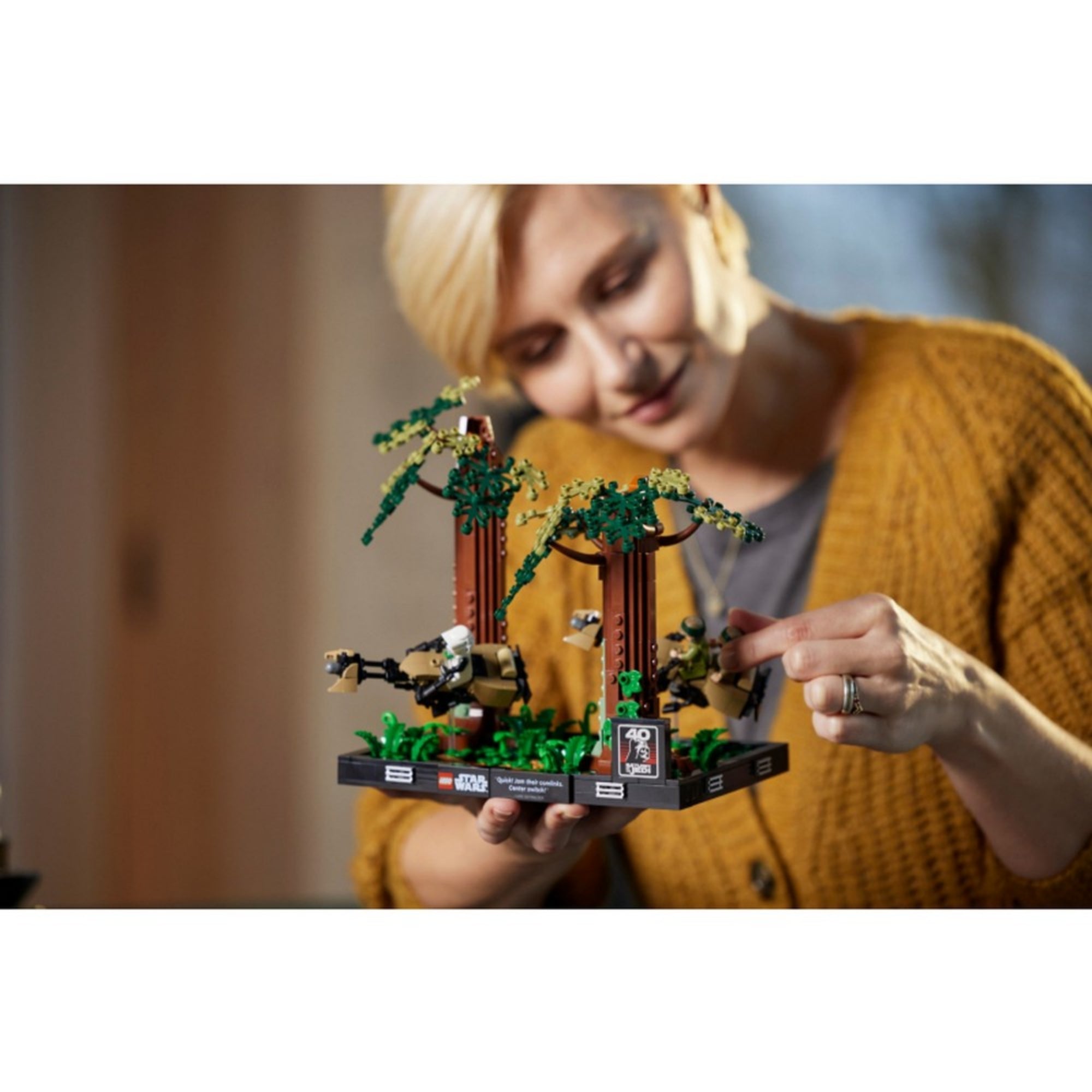 Egy szőke hajú nő kézben tartja és mozgatja a LEGO Endor sikló üldözés diorámát játék közben, jól láthatóak a részletesen kidolgozott fák és figurák.
