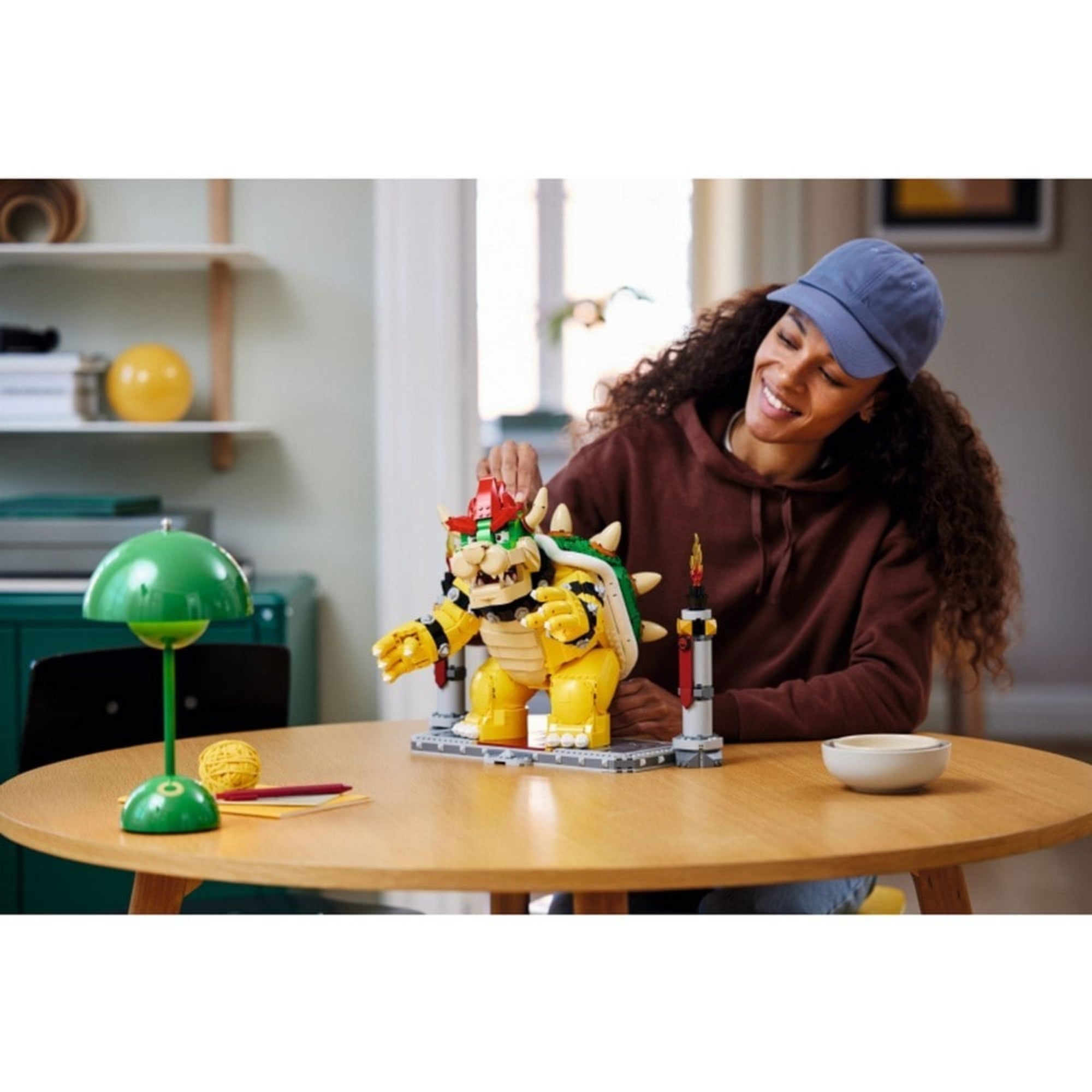 Egy fiatal nő egy asztalnál játszik a LEGO Super Mario A hatalmas Bowser (71411) összeépített figurájával, amely mozgatható végtagokkal és részletgazdag megjelenéssel bír.