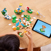 Egy gyerek LEGO Super Mario Big Spike felhőcsúcs kihívás (71409) szettet épít tabletes útmutató segítségével, a darabokat egy asztalon rendezve.
