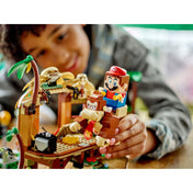 Egy mosolygó kisfiú Mario figurával játszik a LEGO Super Mario Donkey Kong lombháza kiegészítő szettel (71424), miközben Mario Donkey Kong hátán lovagol.