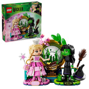 A készlet és a doboz együtt, teljes pompájában: Glinda rózsaszín ruhában, Elphaba fekete öltözetben, varázslatos smaragd háttérrel.