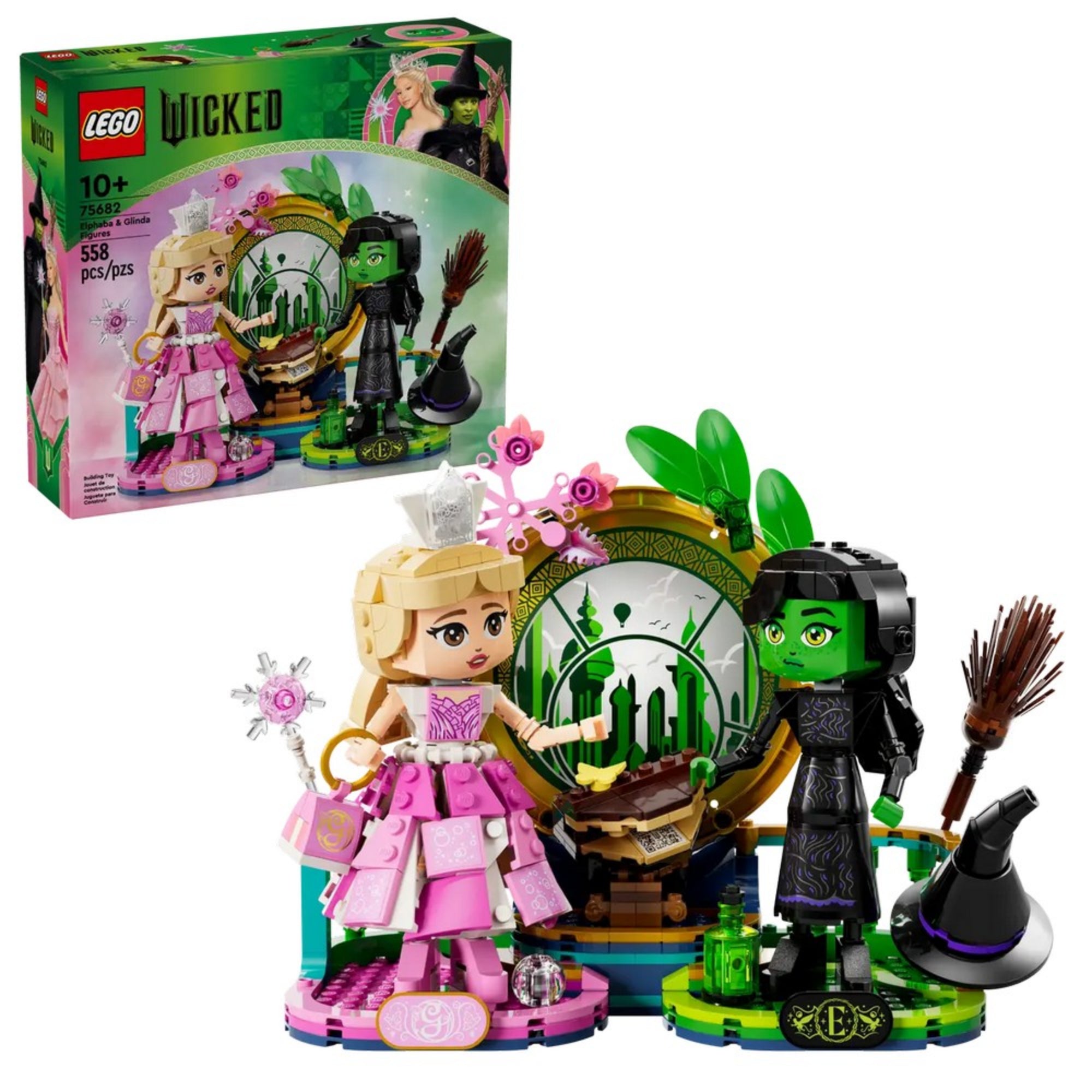 A készlet és a doboz együtt, teljes pompájában: Glinda rózsaszín ruhában, Elphaba fekete öltözetben, varázslatos smaragd háttérrel.