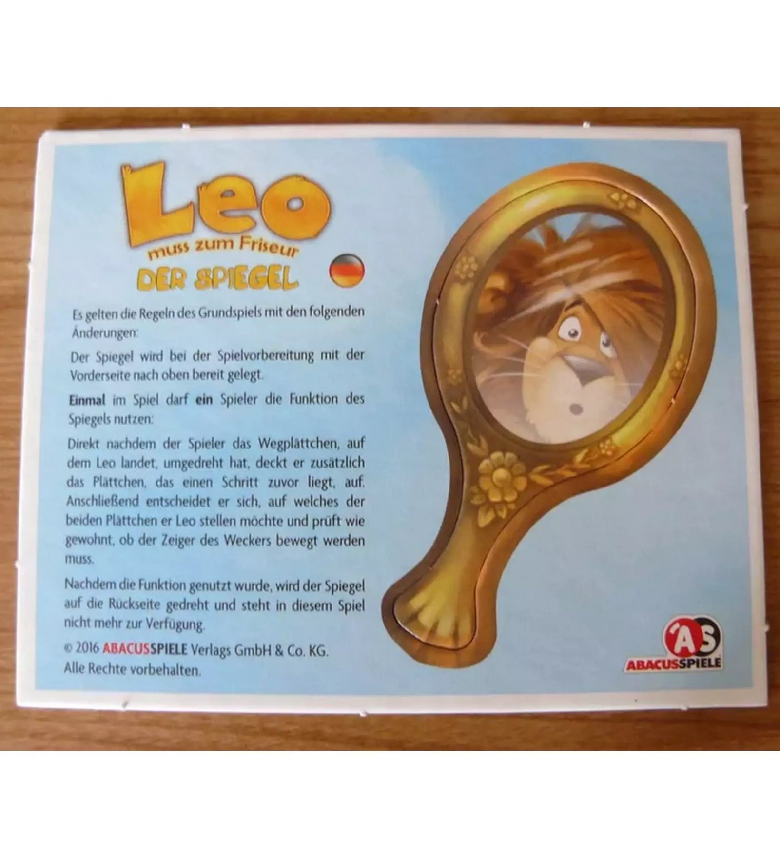 Leo – A tükör kiegészítő német nyelvű szabályleírása. A kép egy aranykeretes kézi tükröt ábrázol, amelyben Leo, az oroszlán tükörképe látható.
