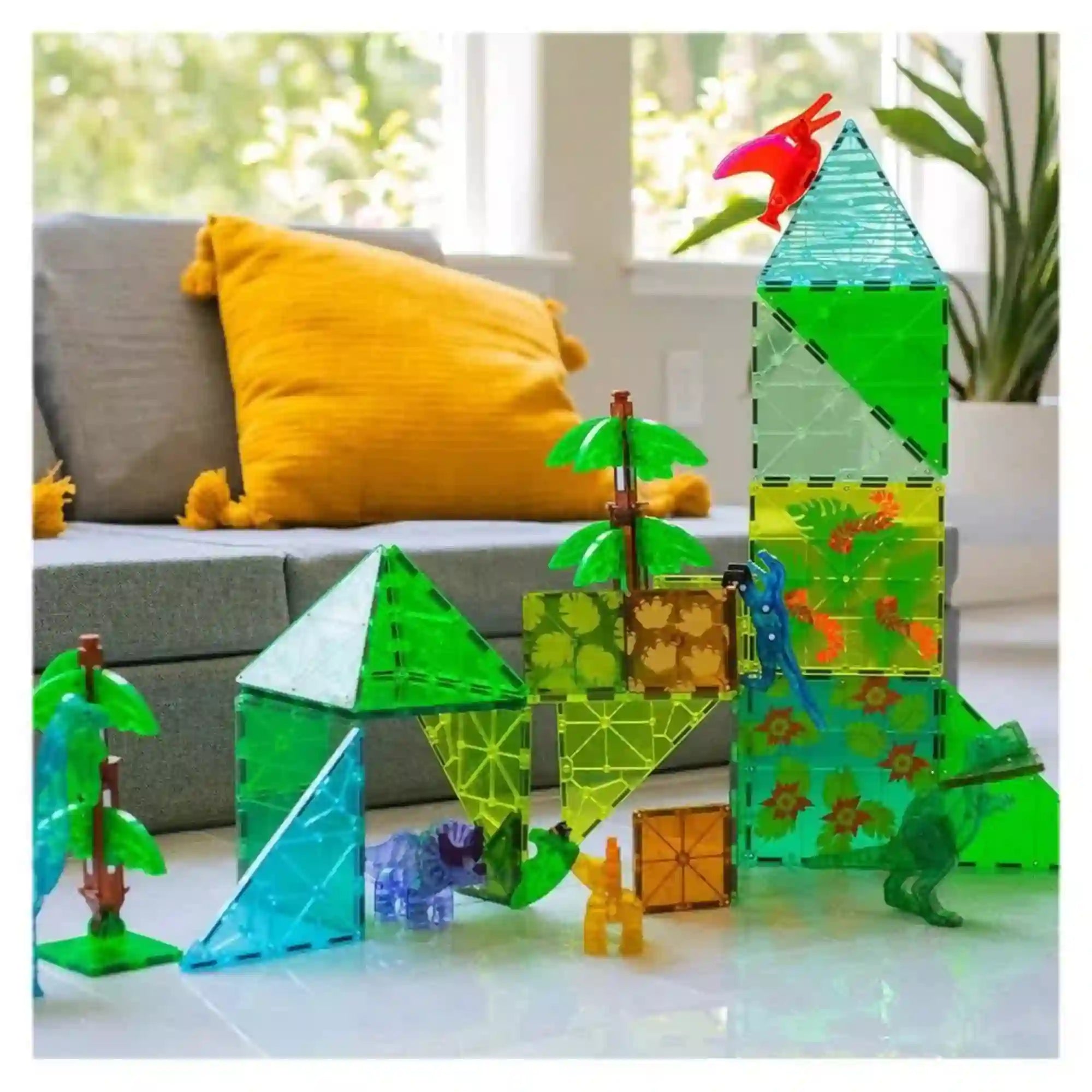 MAGNA-TILES Dino World XL mágneses építőkészletből épített magas dinoszauruszpark, zöld tornyokkal, pálmafákkal és színes dinoszauruszokkal.