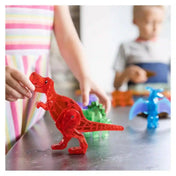 MAGNA-TILES Dino World mágneses építőkészlettel játszó gyermekek, előtérben egy kézzel mozgatott piros T-rex figurával.