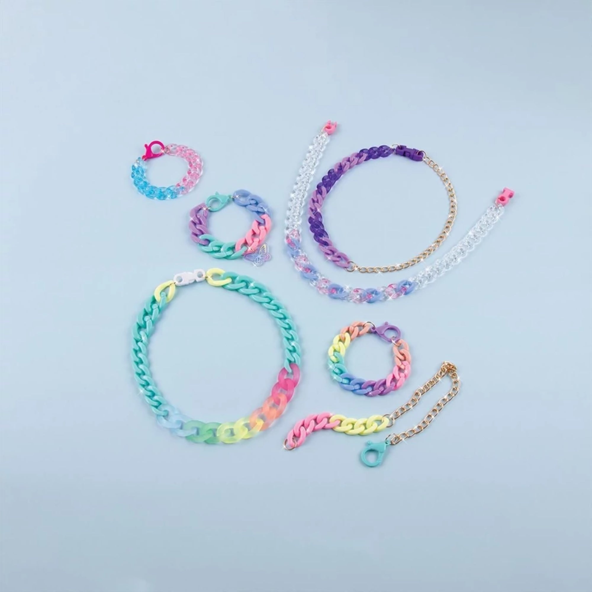 Make It Real lánckarkötő készítő szettből készült szivárványszínű és arany lánc karkötők, változatos mintákkal és csatokkal kék háttéren.