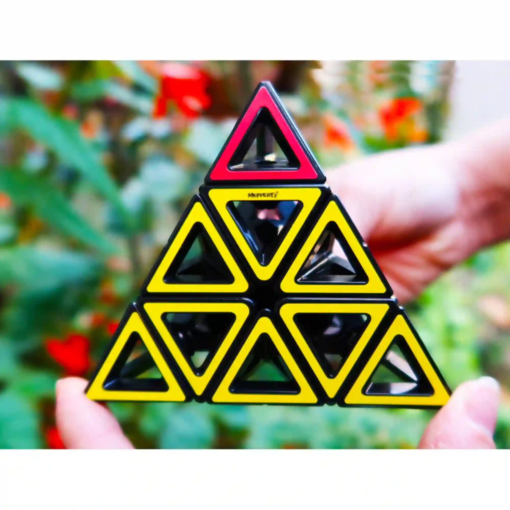 Hollow Pyraminx logikai puzzle sárga és piros háromszög elemekből kirakva, kézben tartva kültéri háttér előtt.