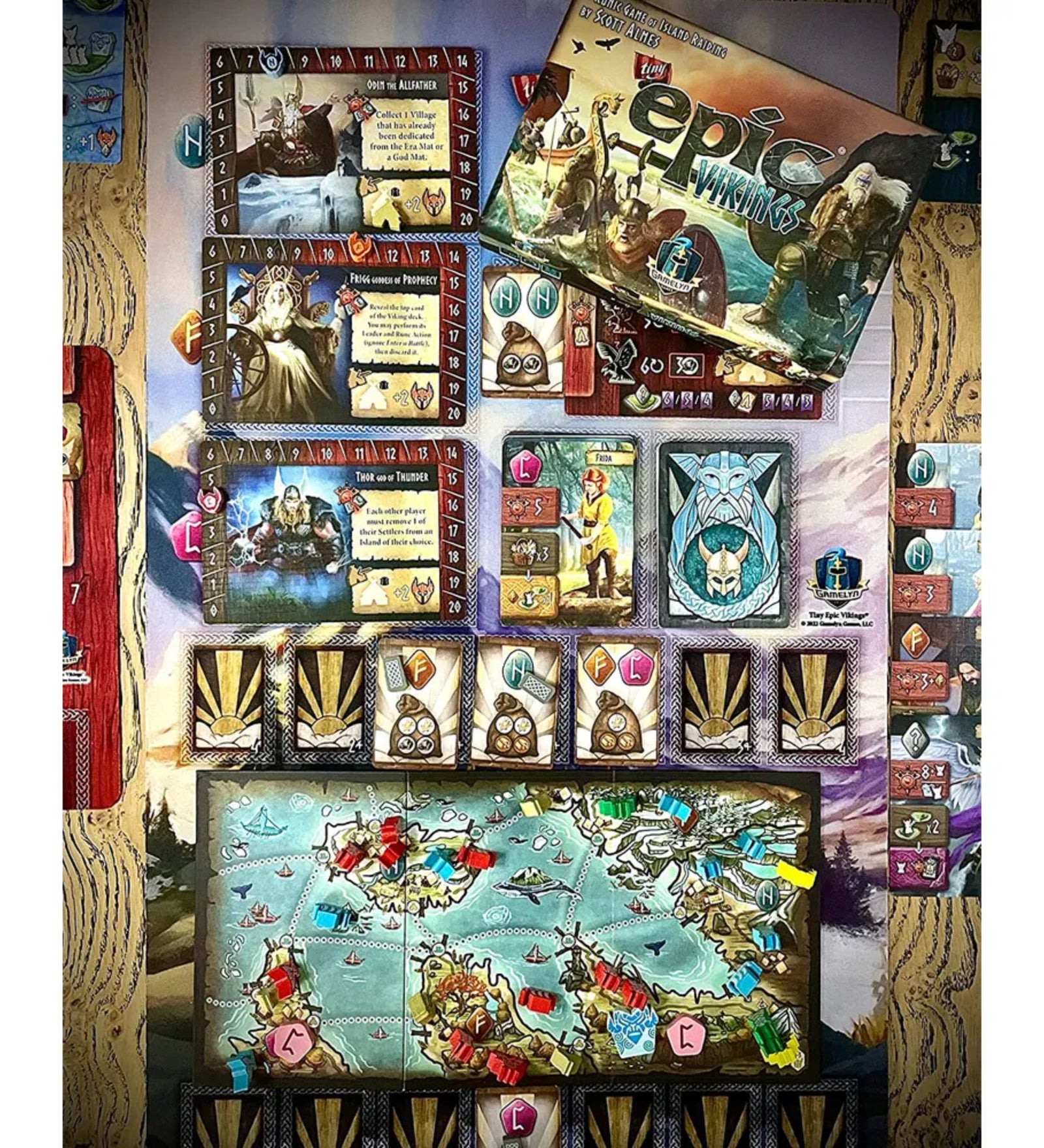  A Tiny Epic Vikings társasjáték elemei játék közben: karakterkártyák, térképlapok, nyersanyagok és jelölők színes, részletes elrendezésben.