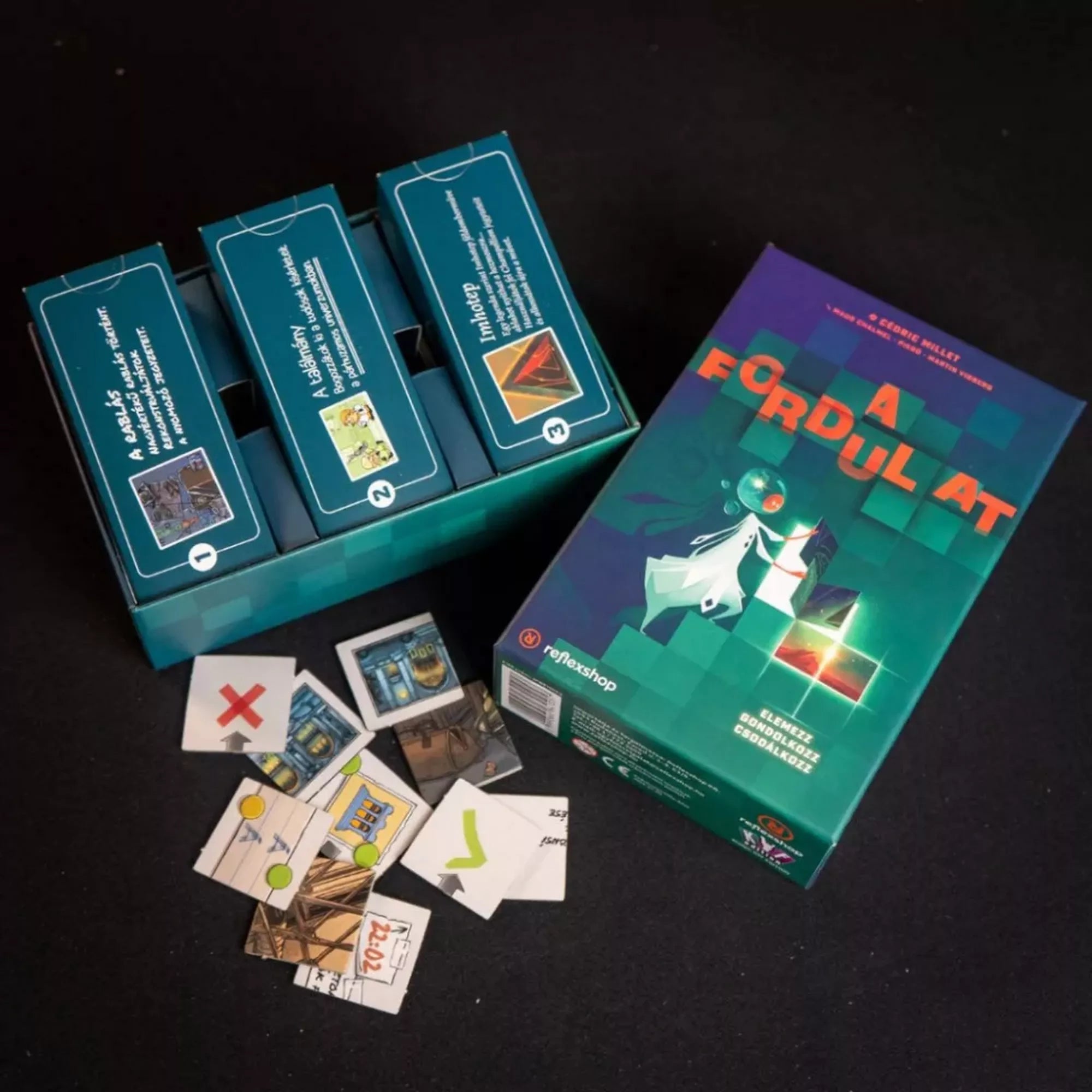 Közelkép A Fordulat társasjáték rekeszeiről és a kirakható lapkákról, amelyeken különböző szimbólumok és illusztrációk láthatók.