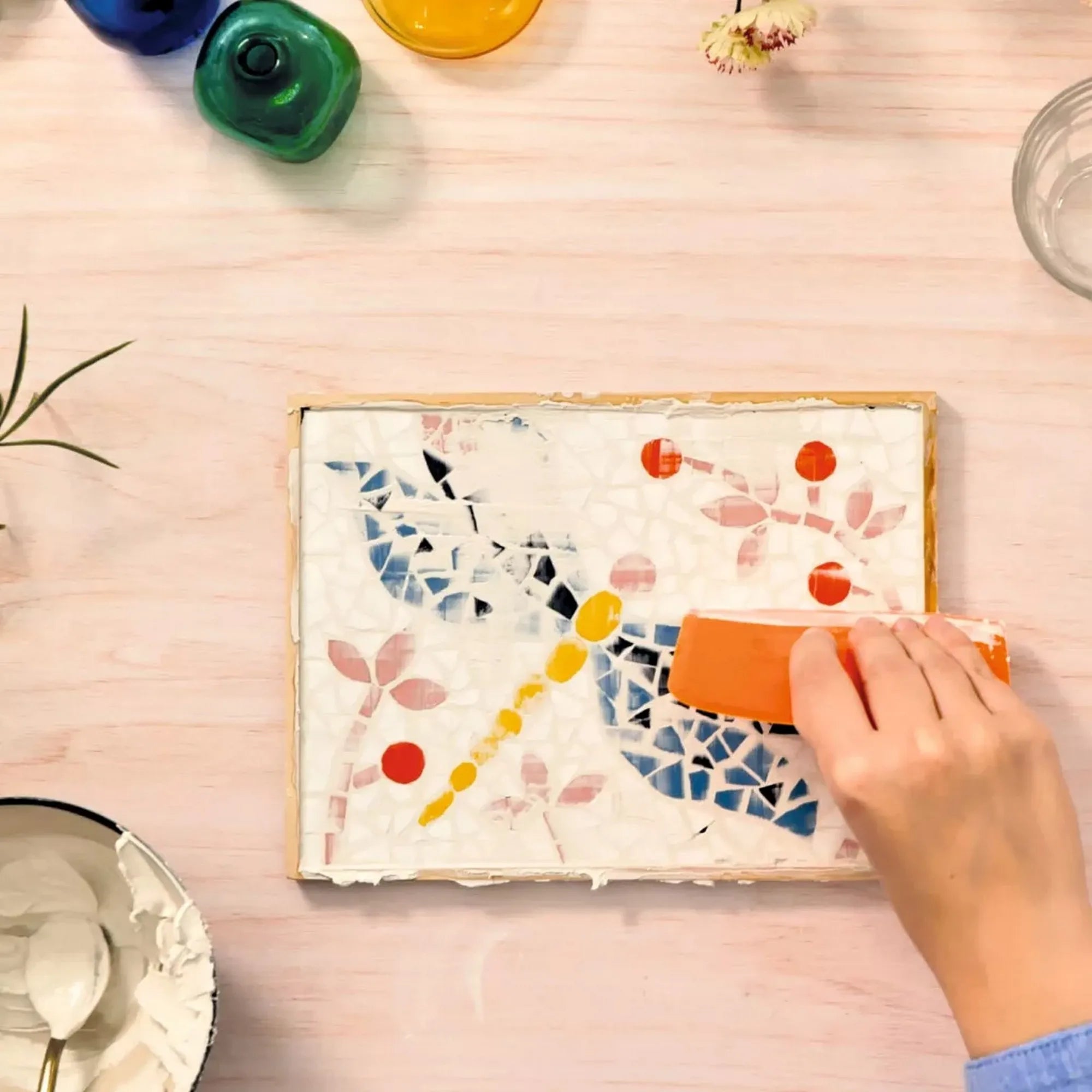 Atelier 72 mozaikkészítő felnőtteknek: Szitakötő – fugázás folyamata narancssárga simítóval a szitakötő mozaikképen.