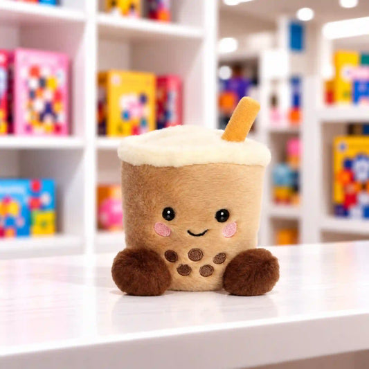 Mosolygós bubble tea plüssfigura barna gyöngyökkel, puha habos tetővel és szívószállal, játékbolti környezetben.
