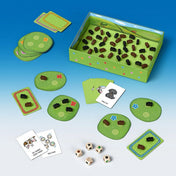 A Bociterelgető játék elemei szétszórva: legelőlapkákon álló bocik, feladatkártyák és több fafigura a dobozban.