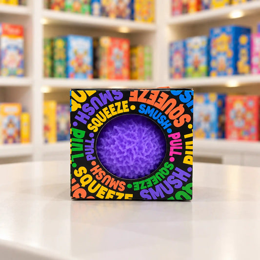 Cool Mix Squishy bolyhos tapintású labda 6 cm stresszlevezető játék (lila), fekete, színes feliratokkal díszített dobozban, kör alakú ablakon keresztül látható.