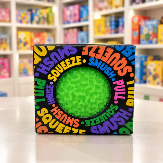 Cool Mix Squishy: Bolyhos tapintású labda 6 cm stresszlevezető játék (zöld), fekete, színes feliratokkal díszített dobozban, kör alakú ablakon keresztül látható.